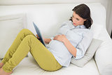 Thinking pregnant brown haired woman using a tablet pc