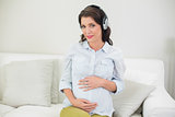 Content pregnant brown haired woman listening to music with headphones