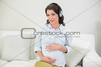 Content pregnant brown haired woman listening to music with headphones