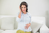 Calm pregnant brown haired woman listening to music with headphones