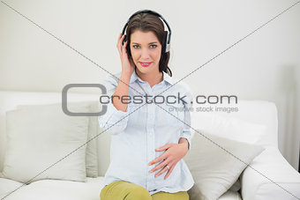 Calm pregnant brown haired woman listening to music with headphones
