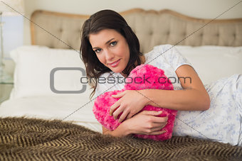 Peaceful pretty brown haired woman hugging a heart shaped pillow