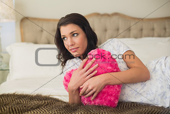 Calm pretty brown haired woman hugging a heart shaped pillow