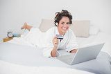 Smiling natural brunette using credit card and laptop