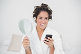 Unsure natural brunette holding mirror and smartphone