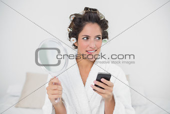 Pensive natural brunette holding mirror and smartphone