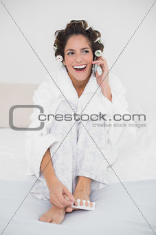 Laughing natural brunette applying nail polish and making a call