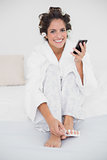 Happy smiling brunette applying nail polish to toes and texting