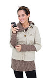 Content cute brunette in winter fashion holding smartphone