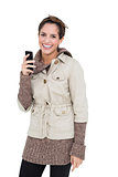 Smiling cute brunette in winter fashion holding smartphone