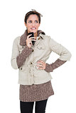 Pensive cute brunette in winter fashion holding smartphone