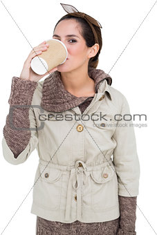 Content cute brunette in winter fashion drinking from disposable cup
