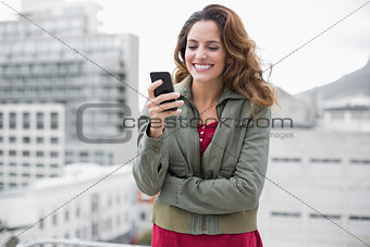 Cheerful gorgeous brunette in winter fashion holding smartphone