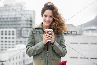 Smiling gorgeous brunette in winter fashion holding disposable cup