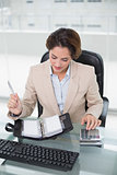 Businesswoman using calculator and looking at diary
