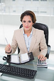 Businesswoman using calculator and diary looking at camera