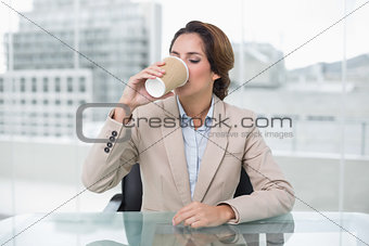 Happy businesswoman sitting at her desk drinking from disposable cup
