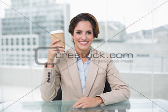 Smiling businesswoman holding disposable cup at her desk