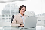 Happy businesswoman typing on laptop at her desk looking at camera