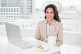 Smiling businesswoman using laptop at her desk and having coffee
