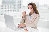 Businesswoman using laptop at her desk and drinking coffee