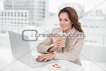 Businesswoman drinking coffee at her desk using laptop