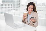 Smiling businesswoman holding disposable cup and smartphone