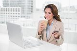 Happy businesswoman holding disposable cup and smartphone