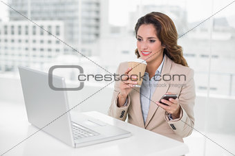 Happy businesswoman holding disposable cup and smartphone