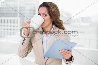 Businesswoman using tablet drinking coffee looking at camera