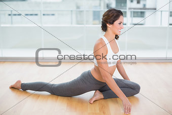 Sporty gleeful brunette stretching on the floor