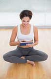 Sporty happy brunette sitting in lotus pose and using tablet