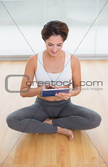 Sporty happy brunette sitting in lotus pose and using tablet