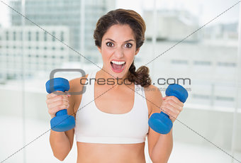 Sporty brunette lifting dumbbells looking at camera