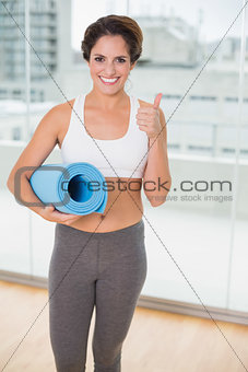 Sporty smiling brunette holding exercising mat