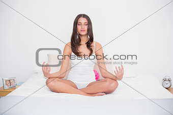 Peaceful young brown haired model in white pajamas practicing yoga