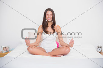 Smiling young brown haired model in white pajamas practicing yoga