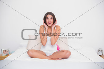 Surprised young brown haired model in white pajamas raising her hands
