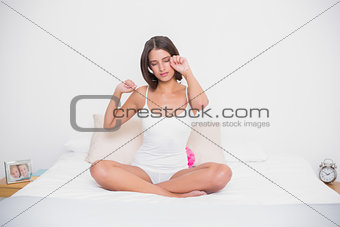Tired young brown haired model in white pajamas stretching her arms