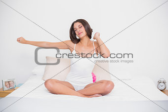 Relaxed young brown haired model in white pajamas stretching her arms