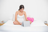 Pleased young brown haired model in white pajamas using a tablet pc