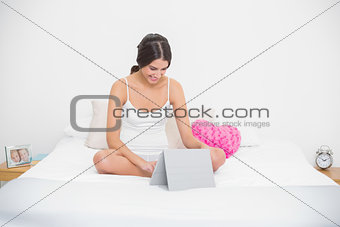 Pleased young brown haired model in white pajamas using a tablet pc