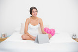 Smiling young brown haired model in white pajamas using a tablet pc