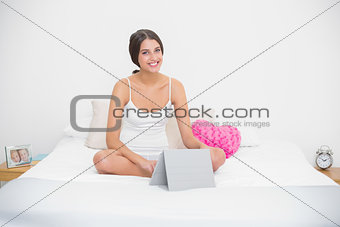 Smiling young brown haired model in white pajamas using a tablet pc