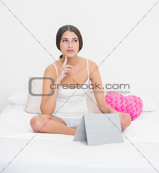Thoughtful young brown haired model in white pajamas using a tablet pc