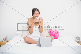 Peaceful young brown haired model in white pajamas enjoying coffee smell