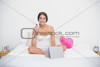Delighted young brown haired model in white pajamas holding a glass of water