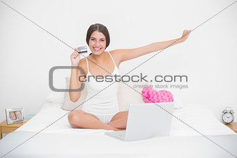 Cheering young brown haired model in white pajamas shopping online with her laptop