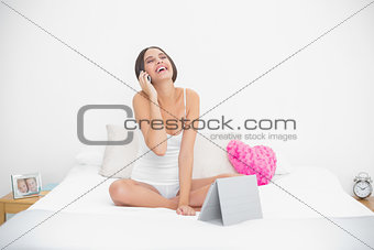 Laughing young brown haired model in white pajamas making a phone call