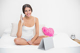 Happy young brown haired model in white pajamas making a phone call